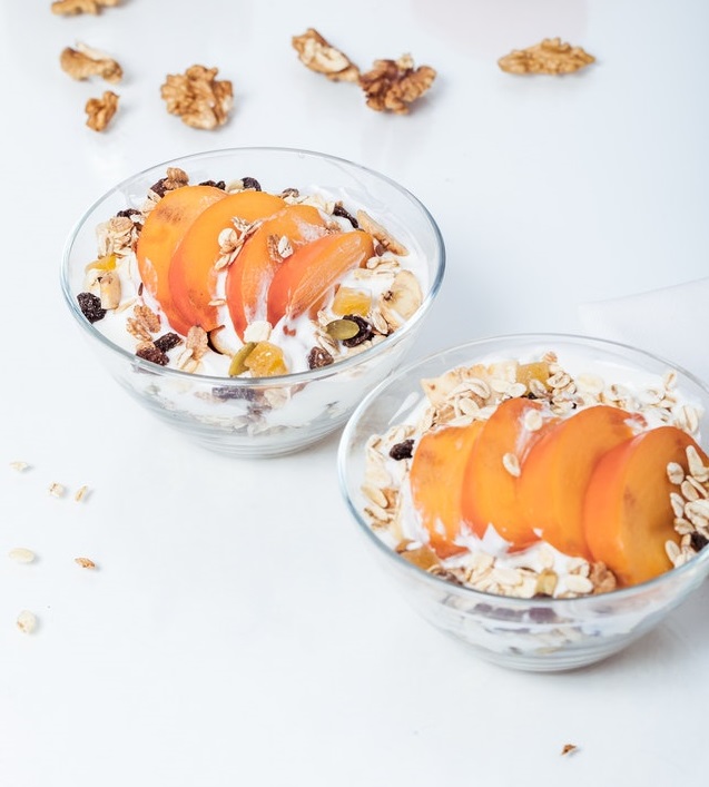 Two bowls of yogurt parfait made with granola and peaches.